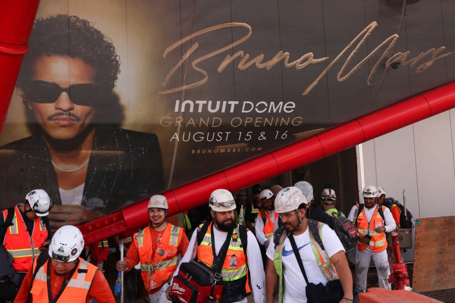 Inglewood, CA – April 17: Construction workers walk outside by a promotion for Bruno Mars performance at Intuit Dome on Wednesday, April 17, 2024 in Inglewood, CA. (Michael Blackshire / Los Angeles Times via Getty Images)