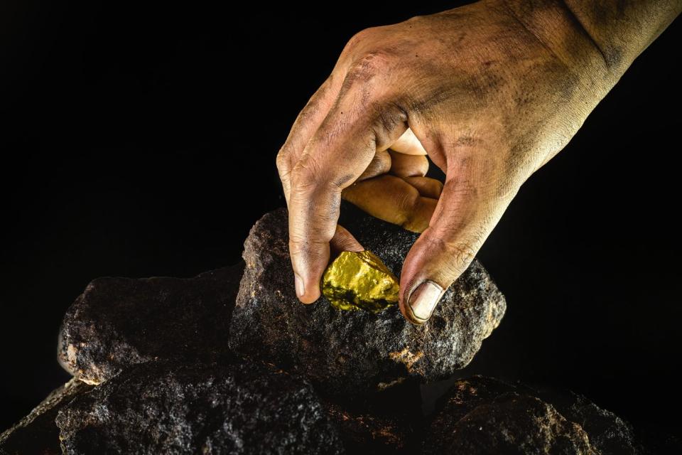 A dirty hand picks up a gold nugget from a pile of soil.