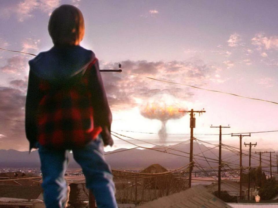 A young boy looking at a nuclear explosion in the distance.