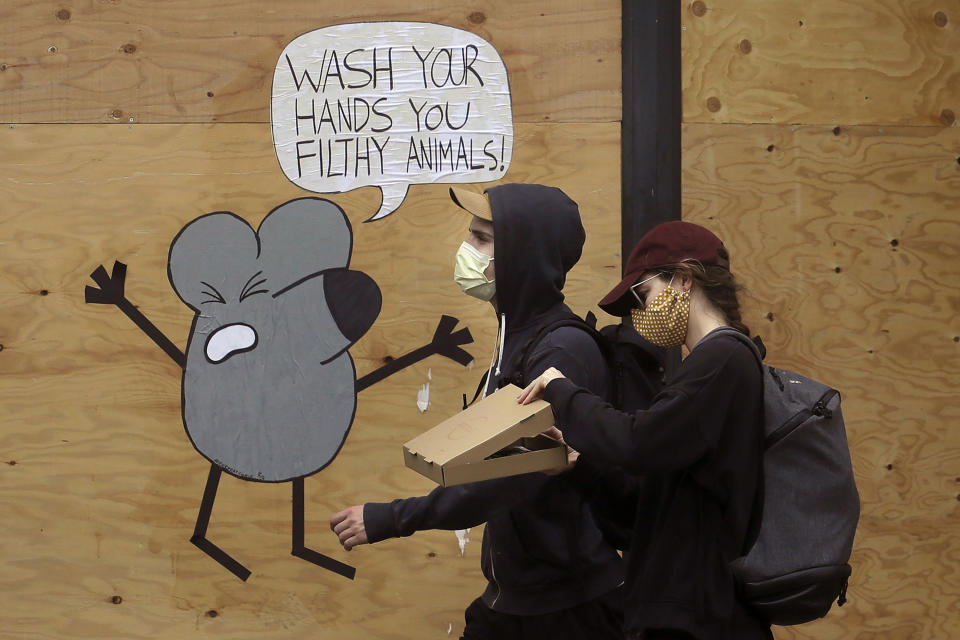 FILE - In this May 2, 2020, file photo, a man and woman wearing masks to prevent the spread of the coronavirus walk past a cartoon advising people to wash their hands on a boarded up storefront in San Francisco. A new analysis published in the journal Lancet on Monday, June 1, 2020, finds masks and social distancing help but hand washing and other measures are still needed to control the coronavirus. (AP Photo/Jeff Chiu, File)