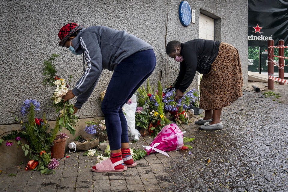 Women place flowers outside the historical home of Anglican Archbishop Desmond Tutu, in Soweto, Johannesburg, South Africa, Monday, Dec. 27, 2021. At midday in Cape Town bells rang from St. George's Anglican Cathedral to honor Archbishop Emeritus Desmond Tutu, a day after his death. (AP Photo/Shiraaz Mohamed)