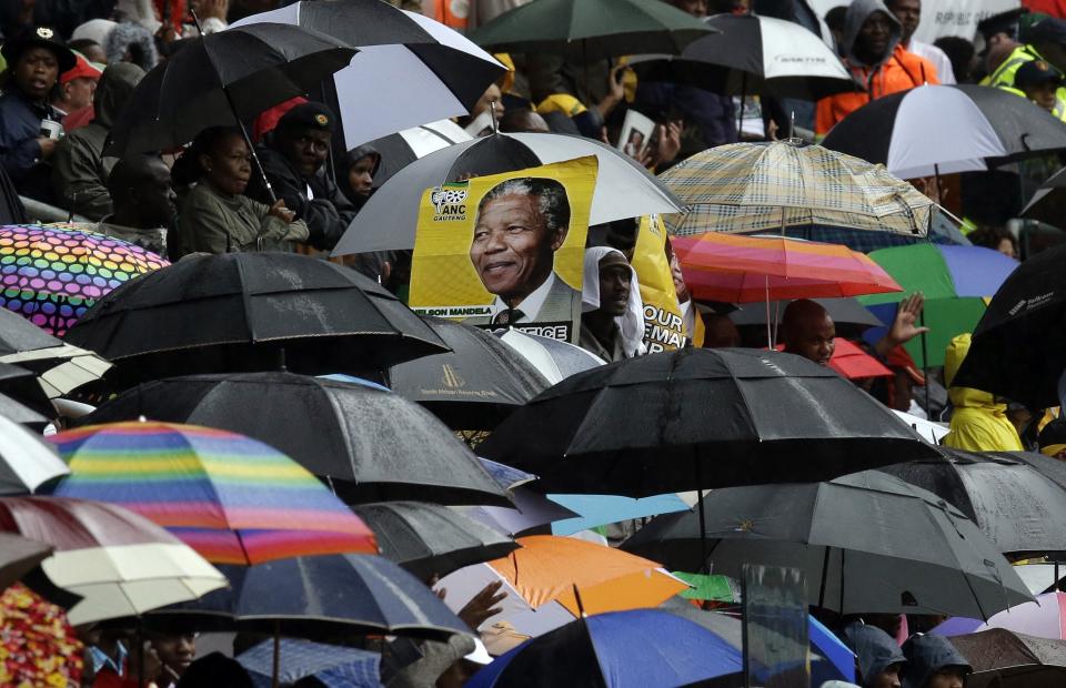 A portrait of Nelson Mandela is seen through a sea of umbrellas during the memorial service for former South African president Nelson Mandela at the FNB Stadium in Soweto, near Johannesburg, South Africa, Tuesday Dec. 10, 2013.(AP Photo/Themba Hadebe)