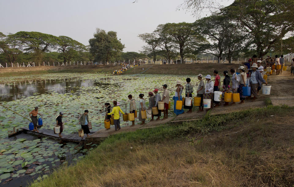 In this April 4, 2014 photo, residents of Dala, carry plastic containers with drinking water as others stand in a line for their turn at a pond in suburbs of Yangon, Myanmar. Every afternoon hundreds of men, women and children stand in a long line waiting to dip their plastic buckets into the lotus-filled pond, their only source of clean drinking water, and during the dry season in April and May, there is only so much to go around.(AP Photo/Gemunu Amarasinghe)