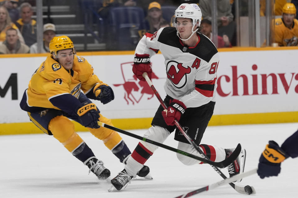 New Jersey Devils center Jack Hughes, right, shoots the puck past Nashville Predators center Mark Jankowski during the first period of an NHL hockey game Tuesday, Feb. 13, 2024, in Nashville, Tenn. (AP Photo/George Walker IV)