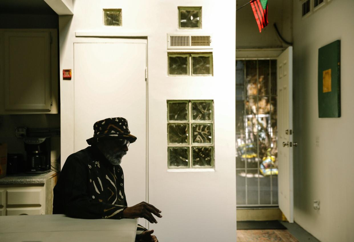 Ulysses Jenkins, wearing a hat, is seen sitting in profile against a white wall lined with glass blocks