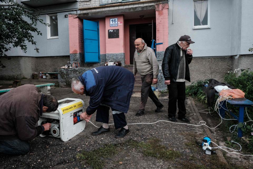 Residents use a generator to charge their mobile phones and flashlights due to a continuous blackout at their apartment building in the frontline town of Kupiansk, Kharkiv region, on Sept. 24, 2022, amid Russia's military invasion of Ukraine. - In the northeastern town of Kupiansk, which was recaptured by Ukrainian forces, clashes continue with the Russian army entrenched on the eastern side of the Oskil river.