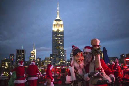 The Empire State Building is seen in the background as revelers taking part in SantaCon are pictured at a top a rooftop bar after sunset in Midtown Manhattan, New York December 13, 2014. REUTERS/Elizabeth Shafiroff