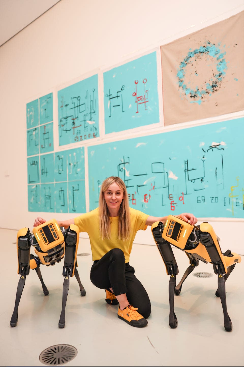Five paintings created by the robot dogs pictured behind Agnieszka Pilat and two robot dogs