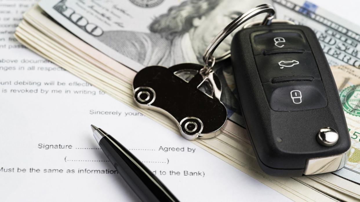 Buy or sell car, purchase or rent automobile service with key with car keychain on pile of US Dollar banknotes money on printed contract paper and pen to sign, finance installment or debt awareness.