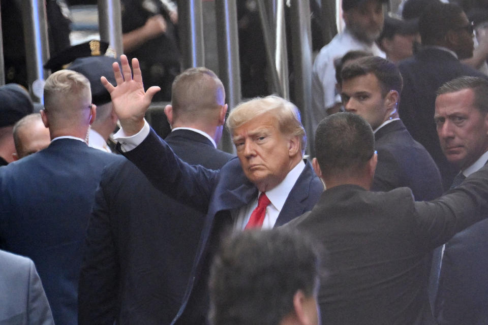 Trump, surrounded by security men, waves as he arrives at the courthouse.