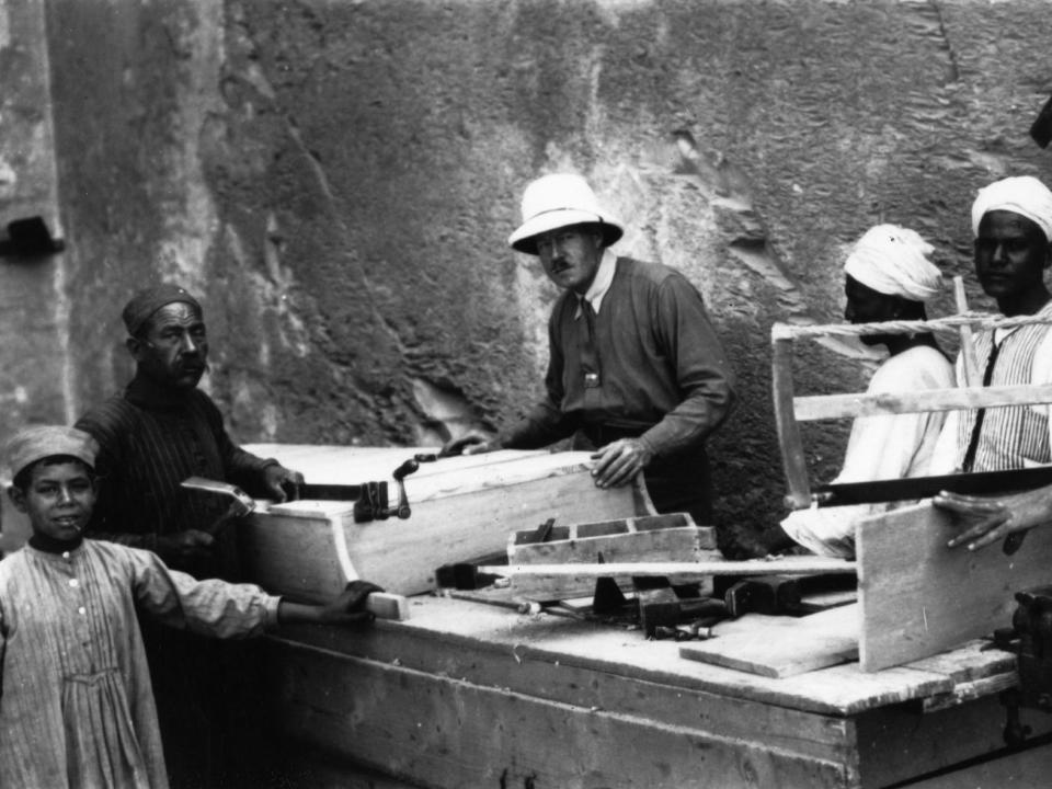 Several men and a boy stand with Howard Carter around a large box with equipment in Tutankhamun's tomb circa 1923.