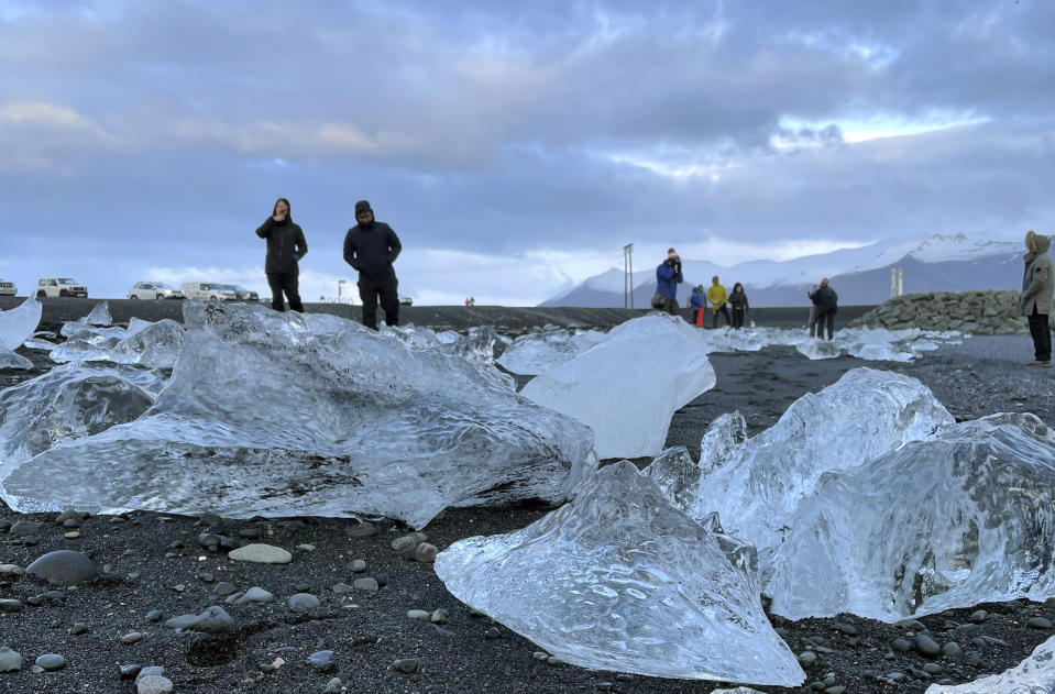 This Nov. 18, 2023 image provided by Beth Harpaz shows visitors amid mini-icebergs on Diamond Beach on Iceland's South Coast. The glistening ice chunks break off from a glacier, float into the Jokulsarlon glacier lagoon and drift onto the volcanic black sand. (Beth Harpaz via AP)