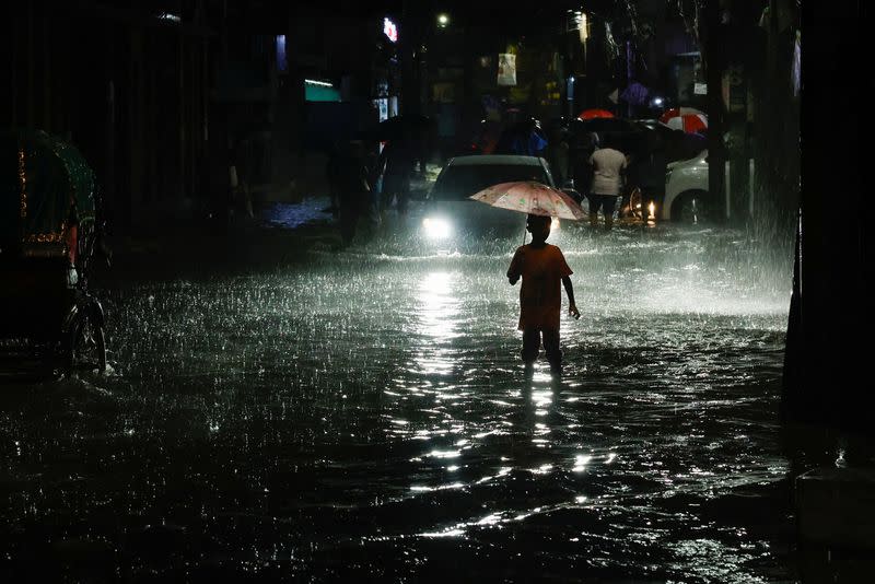 A boy wades through water as streets are flooded due to continuous rain before the Cyclone Sitrang hits in Dhaka