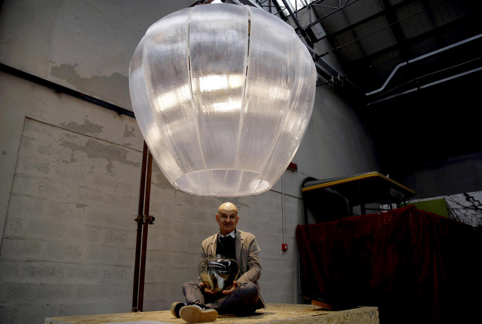 In this picture taken on Thursday, April 11, 2019, designer Tiziano Vudafieri poses under to his creation 'The Wilhem Lamp', made of recycled polycaronate, during the 'RO Master's Pieces exhibition', on the sidelines of the Salone del Mobile International Furniture Fair week, in Milan, Italy. Scientists and environmental activists have been long raised the alarm on plastic pollution. Now, the high-end design world is getting in on the growing global effort to tackle plastic pollution -- by upcycling discarded objects into desirable one-off design pieces. (AP Photo/Luca Bruno)