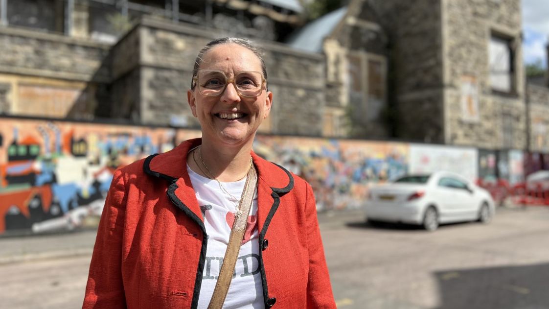 Councillor smiles in front of new murals on the hoardings surrounding the decayed building