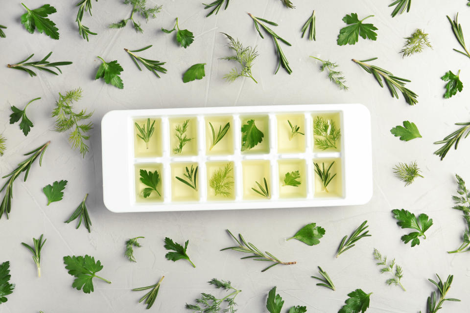 Flat lay composition with ice cube tray and different herbs on grey background