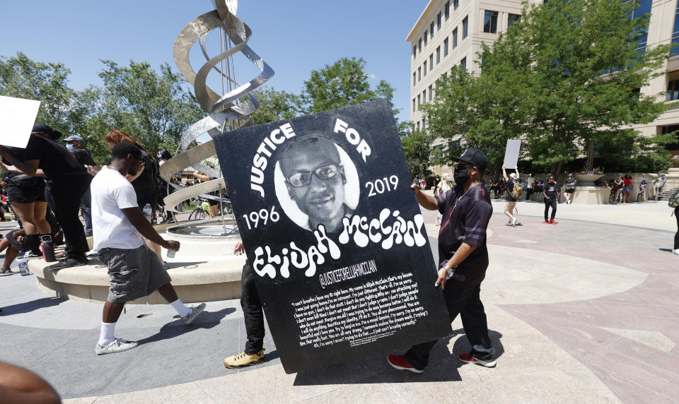 FILE - In this June 27, 2020, file photo, demonstrators carry a giant placard during a rally and march over the death of 23-year-old Elijah McClain outside the police department in Aurora, Colo. Multiple suburban Denver police officers have been placed on paid administrative leave amid an investigation into photos of them related to the case of a Black man who died last summer after he was stopped and restrained, police said Monday, June 29, 2020. The interim police chief of the city of Aurora, Vanessa Wilson, said in a statement that the suspended officers were "depicted in photographs near the site where Elijah McClain died." But her statement did not provide more details about what the images show. (AP Photo/David Zalubowski, File)