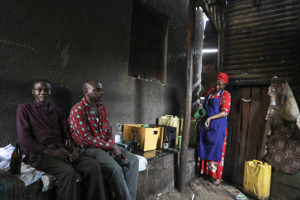 Benson Muhereza, left, an electrical fixer and his friend wait to be served tonto at a local bar in Majengo village in Mbarara, Uganda, Dec. 10, 2023. Tonto is a legendary traditional drink in Uganda. But the fermented banana juice is under threat as authorities move to regulate the production of what are considered illicit home brews. (AP Photo/Hajarah Nalwadda)