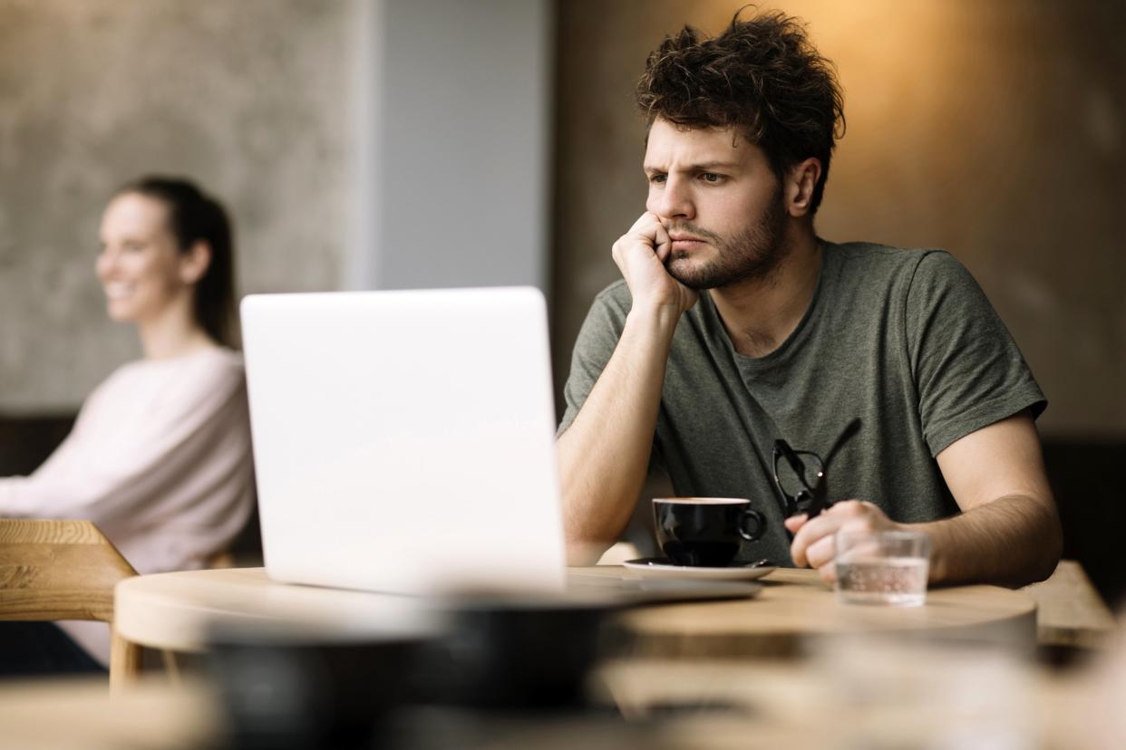 Man in a coffee shop on his laptop looking frustrated