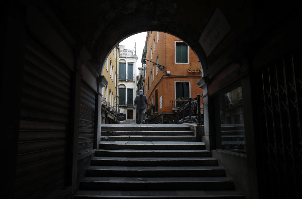 In this picture taken on Wednesday, May 13, 2020, a man wearing a sanitary mask walks in Venice, Italy. Venetians are rethinking their city in the quiet brought by the coronavirus pandemic. For years, the unbridled success of Venice's tourism industry threatened to ruin the things that made it an attractive destination to begin with. Now the pandemic has ground to a halt Italy’s most-visited city, stopped the flow of 3 billion euros in annual tourism-related revenue and devastated the city's economy. (AP Photo/Antonio Calanni)