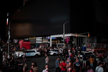 People walk along a dark street near Times Square area, as a blackout affects buildings and traffic during widespread power outages in the Manhattan borough of New York