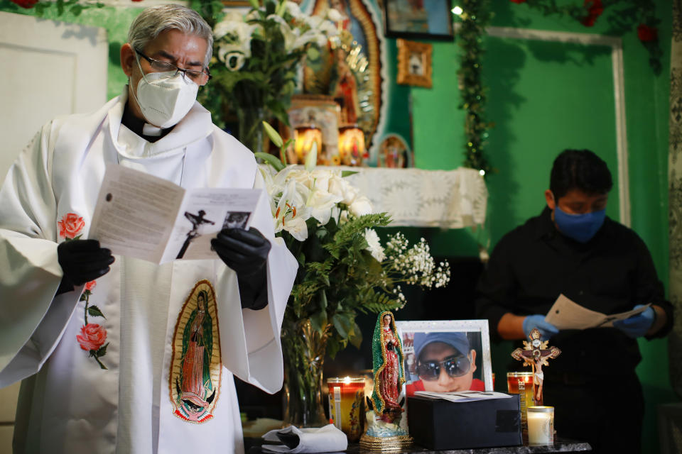 The Rev. Fabian Arias leads a prayer as he performs an in-home service beside the remains of Raul Luis Lopez who died from COVID-19 the previous month, Saturday, May 9, 2020, in the Corona neighborhood of the Queens borough of New York. (AP Photo/John Minchillo)