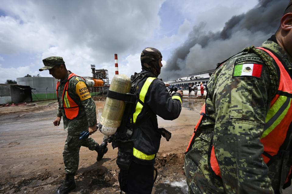 A Cuban firefighter stands between Mexican soldiers as they work to put out a deadly fire at a large oil storage facility in Matanzas, Cuba, Tuesday, Aug. 9, 2022. The fire was triggered when lighting struck one of the facility's eight tanks late Friday, Aug. 5th. (Yamil Lage, Pool photo via AP)