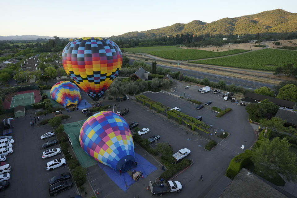 Napa Valley Aloft hot air balloons prepare to lift off in Yountville, Calif., Monday, June 19, 2023. This year, wine grapes are thriving after a winter of record amounts of rain fell in California, but a recent trip high above the valley in a hot air balloon revealed miles of lush, green vineyards — the only blemish coming from shadows cast by the balloons themselves. (AP Photo/Eric Risberg)