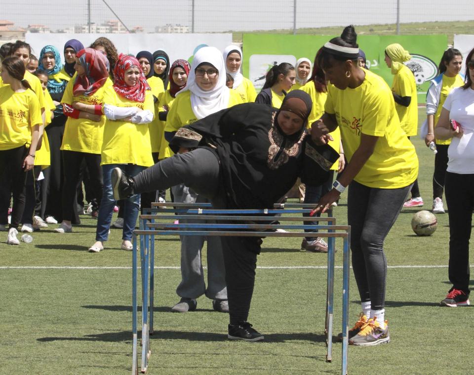American track and field great Jackie Joyner-Kersee helps a Palestinian woman over a hurdle in the West Bank city of Ramallah, Thursday, April 17, 2014. The three-time Olympic gold medalist visited the West Bank to encourage Palestinian women to be physically active. (AP Photo/Nasser Shiyoukhi)