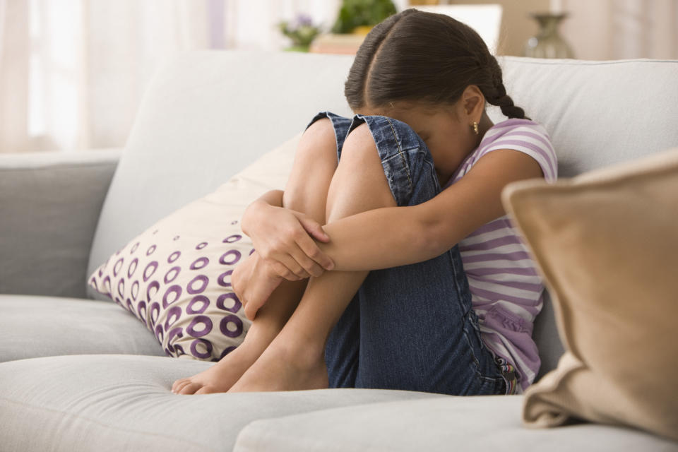 Sad Hispanic girl sitting on sofa