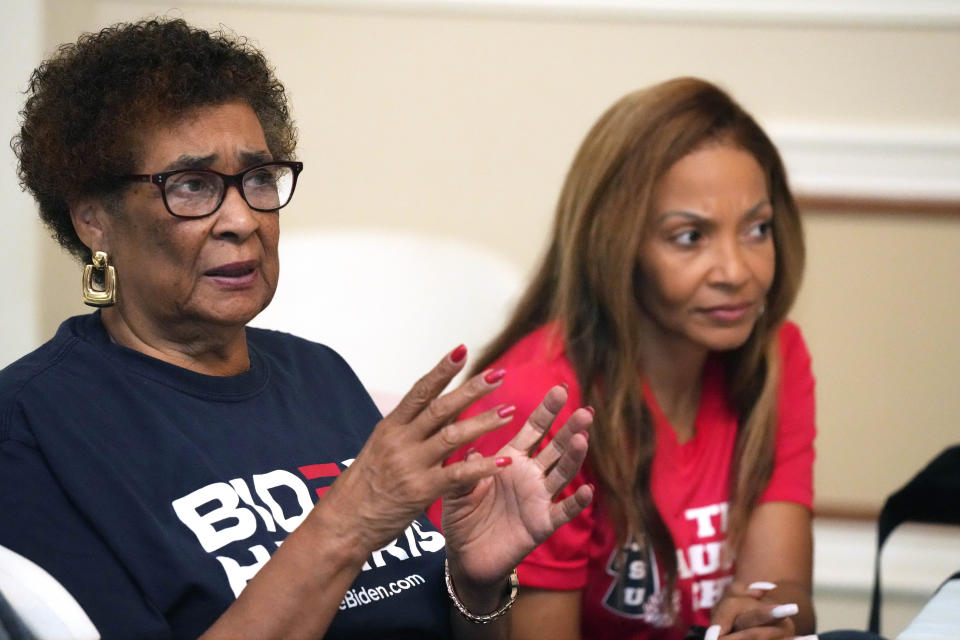 Two women wearing Biden-Harris campaign shirts, engaged in discussion, sitting at a table