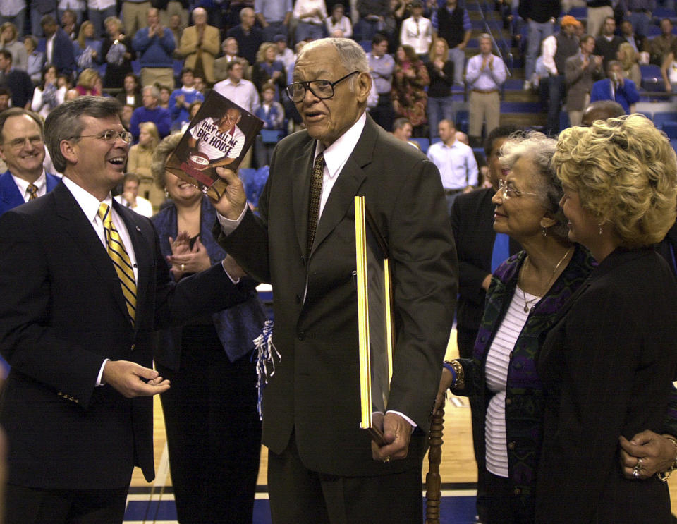 FILE - Clarence "Big House" Gaines, center, gives Kentucky Gov. Ernie Fletcher, left, a copy of his book "They Call Me Big House" after Fletcher and the University of Kentucky honored the Paducah, Ky. native as the all-time winningest coach in NCAA Division II during halftime ceremonies at Rupp Arena in Lexington, Ky., Sunday, Jan. 9, 2005. Gaines had 828 victories in 47 years at Winston-Salem State University. Looking on at right is Clara Gaines, his wife of 50 years, and Glenna Fletcher, far right. (AP Photo/Garry Jones, File)