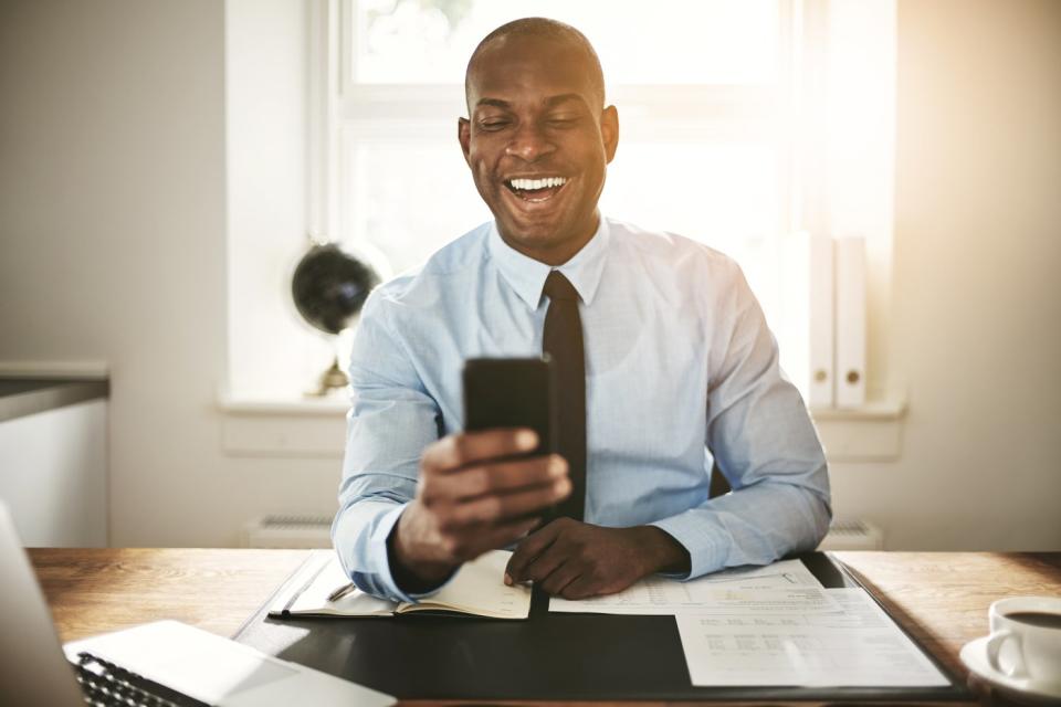 Investor smiling while looking at phone in office.