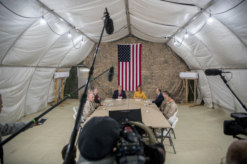President Donald Trump, accompanied by National Security Adviser John Bolton, third from left, first lady Melania Trump, fourth from right, U.S. Ambassador to Iraq Doug Silliman, third from right, and senior military leadership, speaks to members of the media at Al Asad Air Base, Iraq, Wednesday, Dec. 26, 2018. (AP Photo/Andrew Harnik)