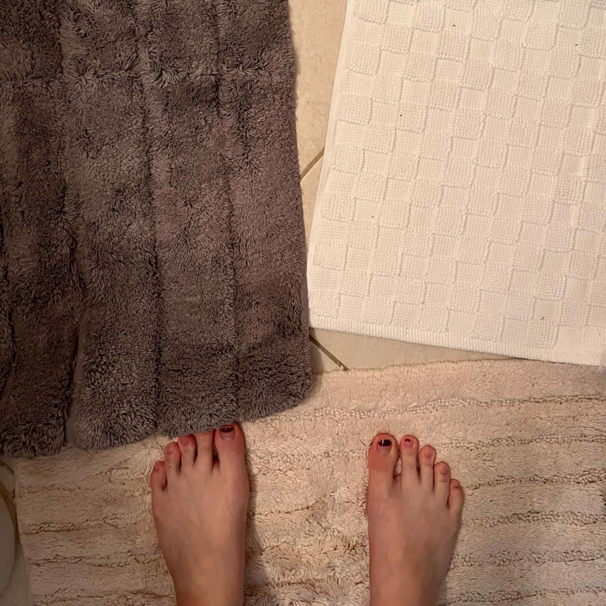 Person stands with feet showing on fluffy beige bath mat with a fluffy brown and checkered white one in front of her. (Courtesy Lauren Swanson)