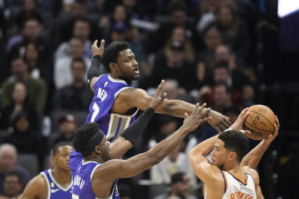 Sacramento Kings forward Chimezie Metu (7) and guard Terence Davis, front bottom left, defend against Phoenix Suns guard Devin Booker, right, in the first quarter in an NBA basketball game in Sacramento, Calif., Friday, March 24, 2023. (AP Photo/José Luis Villegas)