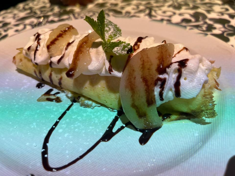 a crepe with whipped cream, pears, and chocolate sauce on white plate at Le Petit Chef