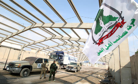 Members of Shi'ite group Asaib ahl al-Haq walk outside their premises in Basra, Iraq November 8, 2018. The text on the flag reads: 'Asaib ahl al-Haq Movement'. Picture taken November 8, 2018. To match Insight IRAQ-MILITIAS/ REUTERS/Essam al-Sudani