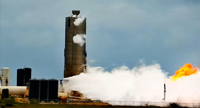 The Starship prototype vents clouds of vapor after a presumably successful engine test firing while gas from methane propellant is released from a flare stack, at right. / Credit: LabPadre