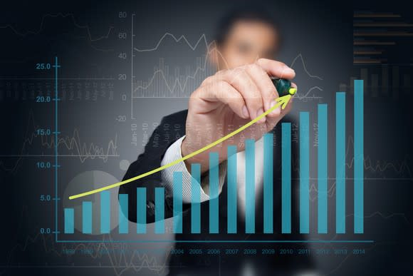 A man drawing a rising line over a bar chart that heads higher