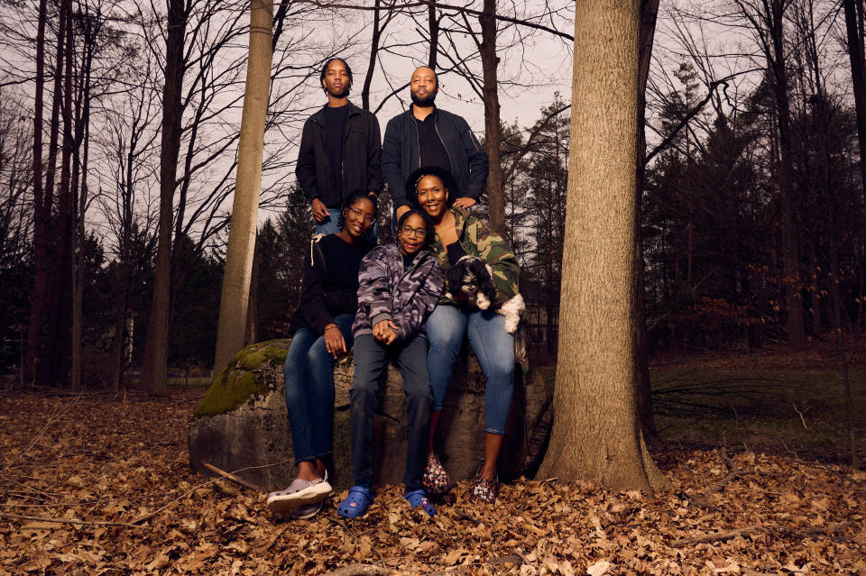 Family with two adults and three children, one holding a dog, posing together in a wooded area