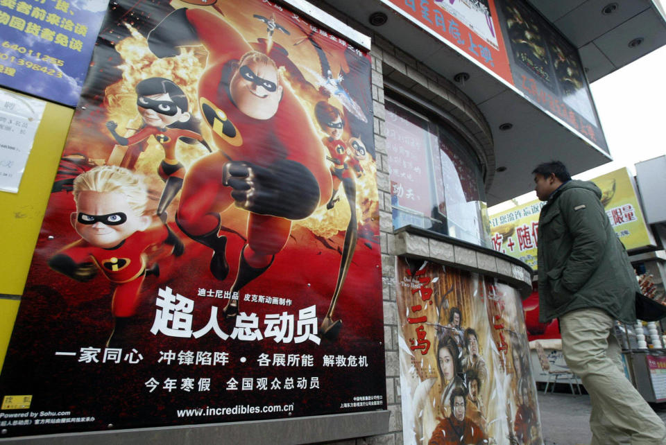 A young man looks at a poster showing five animated characters in red jumpsuits and black masks.