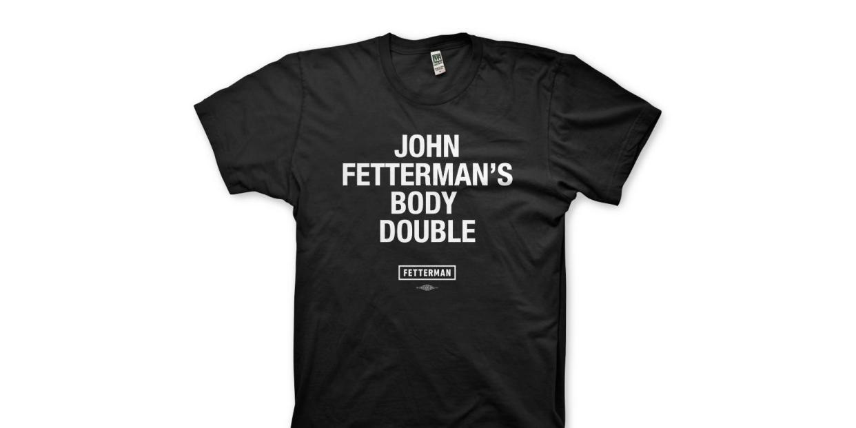 A black T-shirt with white lettering which says, "John Fetterman's Body Double"