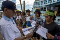 Migrant workers hold up their identity cards as a Thai authority officer checks them at a port in Samut Songkhram province, Thailand, July 1, 2015. REUTERS/Athit Perawongmetha