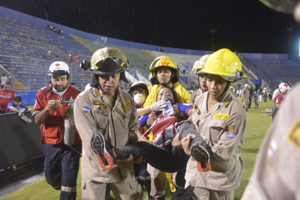 Firefighters carry away a fan affected by tear gas fired by police to break up deadly fights between fans before the start of a game between Motagua and Olimpia inside the national stadium in Tegucigalpa, Honduras, on Saturday.