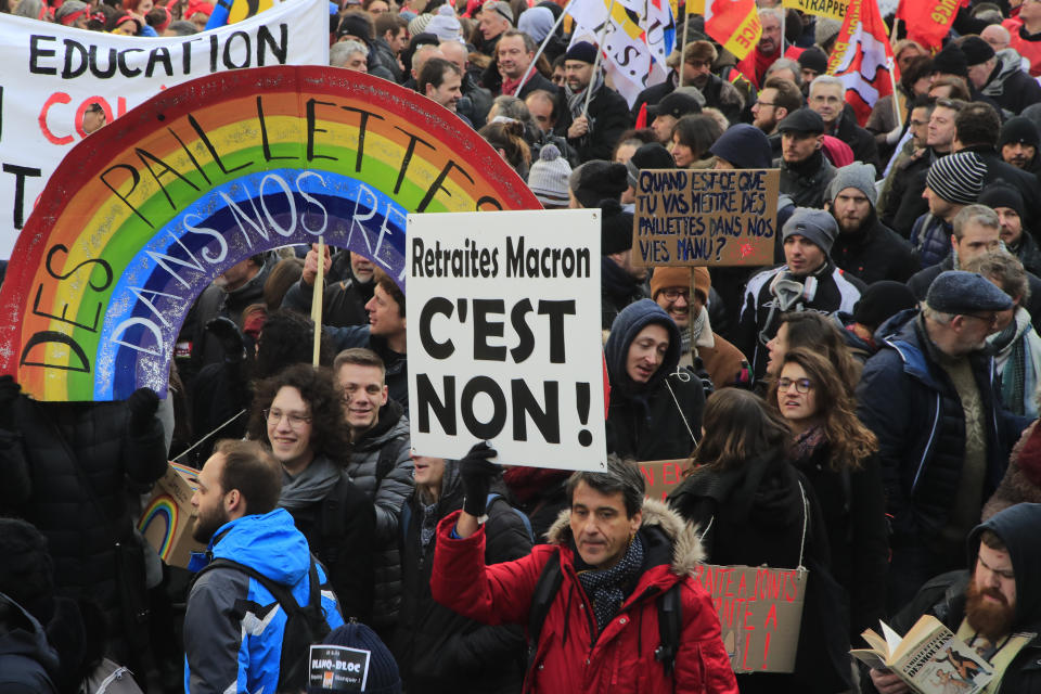 Protesters march, one with a poster reading "Macron's reform, it's No" during a demonstration, Friday, Jan. 24, 2020 in Paris. French unions are holding last-ditch strikes and protests around the country Friday as the government unveils a divisive bill redesigning the national retirement system. (AP Photo/Michel Euler)