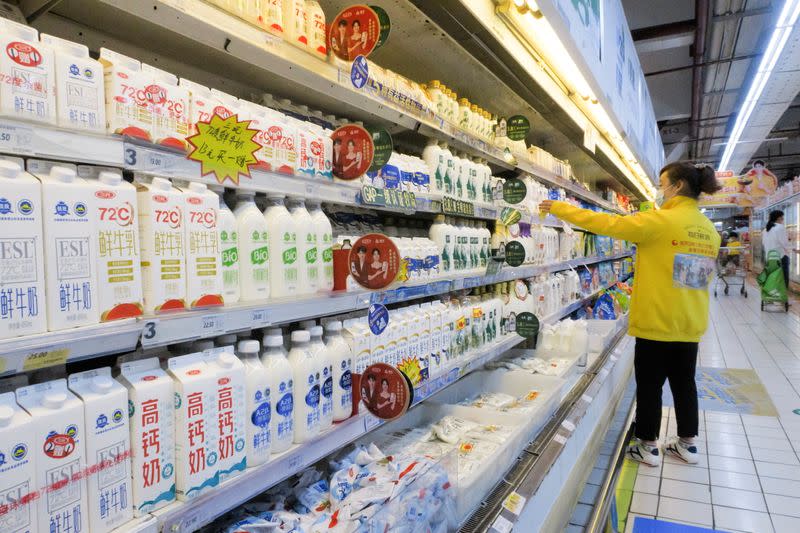 Staff member arranges cartons of milk on refrigerator shelves at a supermarket in Beijing