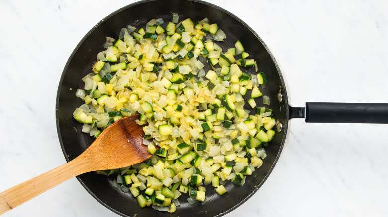 Diced onion and zucchini frying in pan