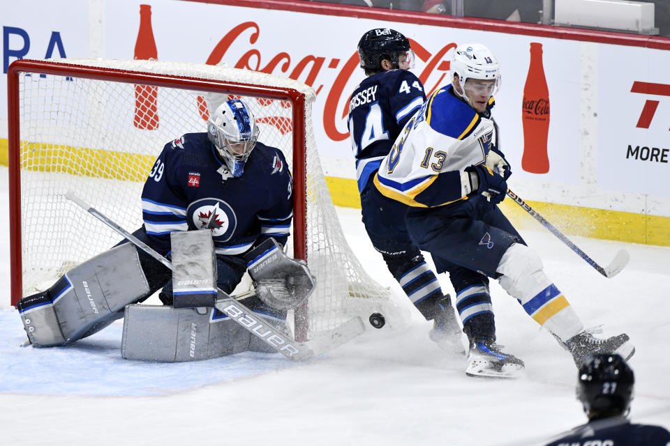 St. Louis Blues' Alexey Toropchenko (13) is checked by Winnipeg Jets' Josh Morrissey (44) near goaltender Laurent Brossoit (39) during the third period of an NHL hockey game Tuesday, Feb. 27, 2024, in Winnipeg, Manitoba. (Fred Greenslade/The Canadian Press via AP)