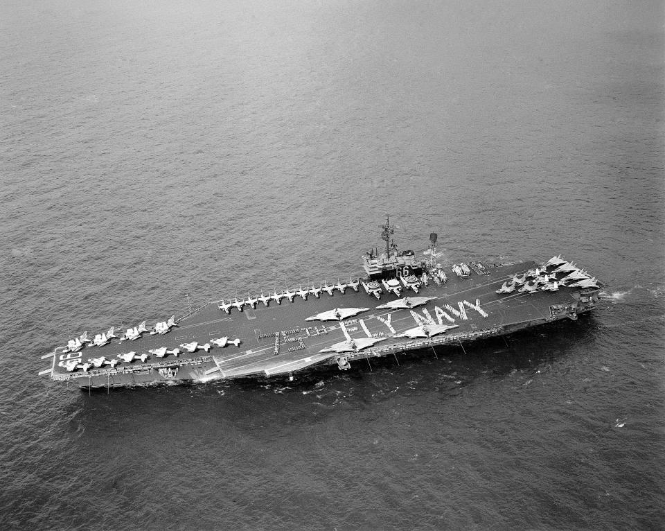 Crewmen and aviators on the aircraft carrier USS America (CV 66) stand in a reading formation "75th Fly Navy" on the flight deck